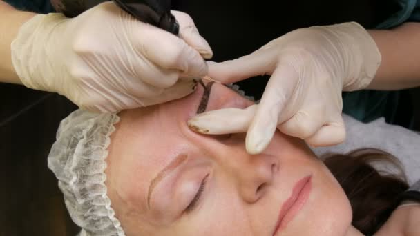 Pen with a needle for permanent make-up, the master hands make correction of the shape of eyebrows in the beauty parlor. Modern method of correction with powder spraying. Microblading, eyebrow tattoo - Footage, Video