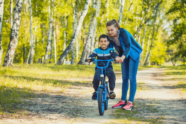 Happy kid cyclist learning to ride a bike with mom in the sunny forest on a bike - Zdjęcie, obraz