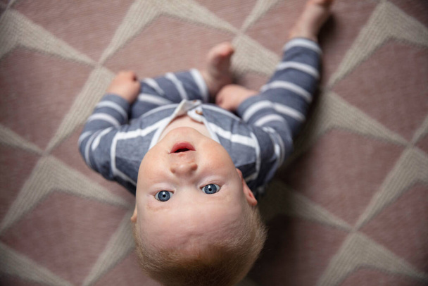 A cute baby boy sat on a nursery floor looking up to the camera - Фото, зображення