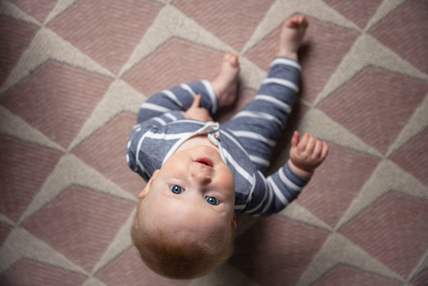 A cute baby boy sat on a nursery floor looking up to the camera - Foto, imagen