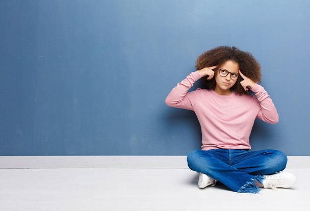 african american little girl looking concentrated and thinking hard on an idea, imagining a solution to a challenge or problem sitting on the floor - Photo, image