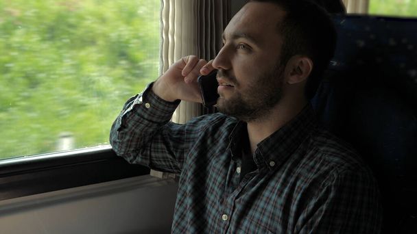 Handsome man talking on mobile phone in train. - Zdjęcie, obraz