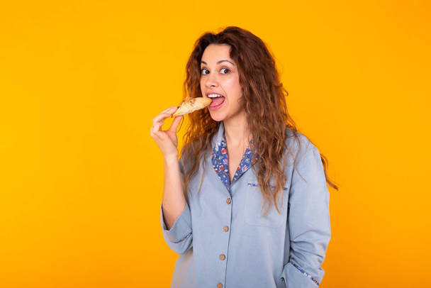 Fröhliche Frau trägt Pyjama Mode gehen kleine leckere Croissants auf gelbem Hintergrund zu essen. Morgen-, Frühstücks- und Home Wear-Konzept. - Foto, Bild