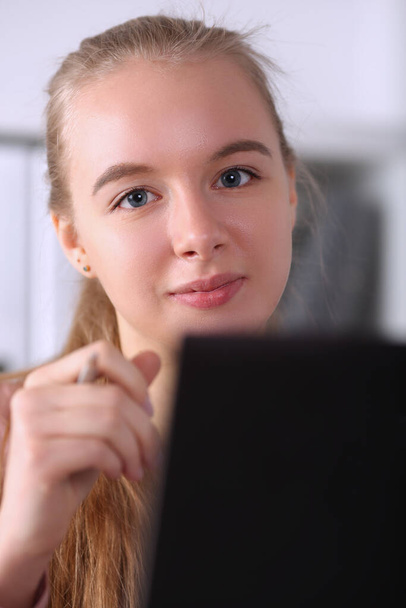 Kaunis tyttö pitää kynää istuu kannettavan tietokoneen vieressä
 - Valokuva, kuva