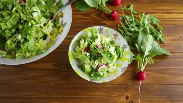 Spring salad from early vegetables, lettuce leaves, radishes and herbs in a plate on the wooden table - Video