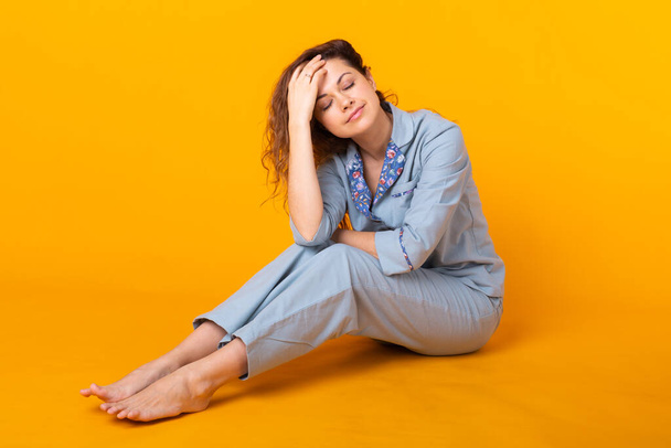 Smiling young girl in pajamas home wear posing while resting at home isolated on yellow background studio portrait. Relax good mood lifestyle concept. - Photo, Image