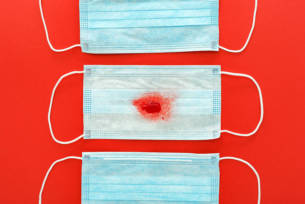 Hemoptysis, coronavirus, protective surgical masks with blood on red background. Pneumonia, acute respiratory infections, tuberculosis, lung cancer, hemoptysis, epidemic. Chinese coronavirus 2020 - Photo, Image