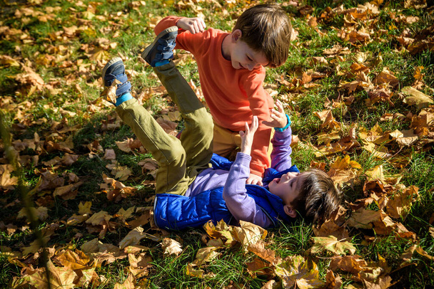 Two boys fighting outdoors. Friends wrestling in summer park. Siblings rivalry. Aggressive kid hold younger boy on ground, try to hit him. - Foto, imagen