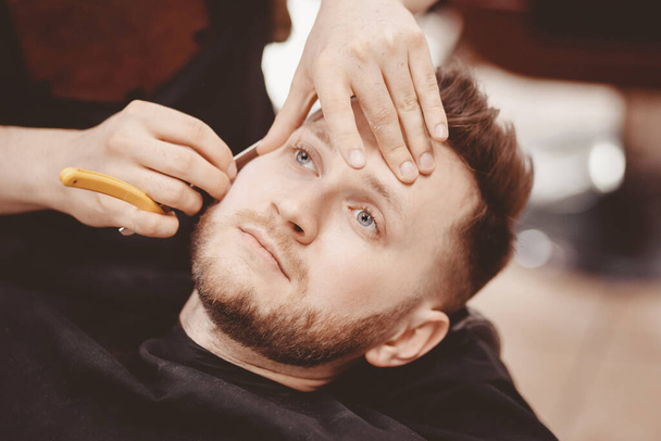 Мужчина парикмахер бреет бороду клиента на стуле Парикмахерской
 - Фото, изображение