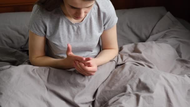 Tired young woman sitting on bed massaging hand suffering from rheumatoid arthritis concept, girl patient touching wrist feeling hurt joint pain having osteoarthritis disease health problem - Filmati, video