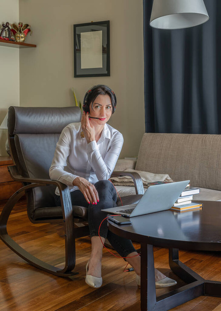 Woman working in home office during corona virus (COVID-19) outbreak talking with headphones on - Valokuva, kuva