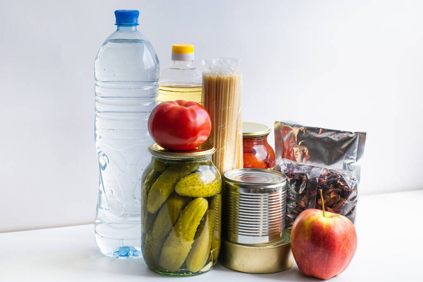 Donation for food delivery. Help with products during a crisis. Canned meat and fish, pickled tomatoes and cucumbers, vegetable oil, pasta, tea, water, apple, tomato. Coronavirus quarantine. - Foto, afbeelding