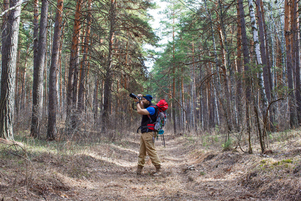バードウォッチャーはカメラを持って森を歩き、鳥の写真を撮る - 写真・画像