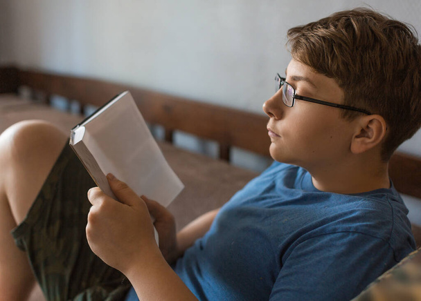 Nastolatek w okularach czyta książkę w domu. - Zdjęcie, obraz