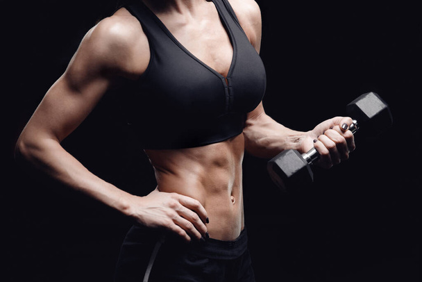 Fitnesskonzept, Training. Sportliche junge Frau auf isoliertem schwarzem Hintergrund mit Hanteln in der Hand - Foto, Bild