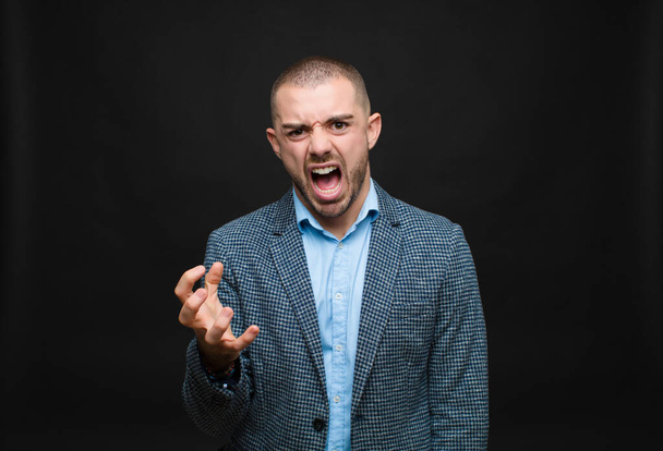 young businessman looking angry, annoyed and frustrated screaming wtf or whats wrong with you against flat wall  - Foto, afbeelding