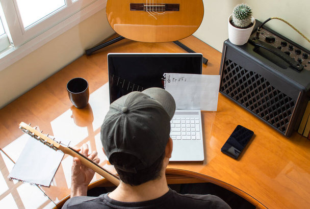 Guitarrista tocando y aprendiendo guitarra eléctrica usando un portátil en casa. Músico en su habitación practicando la guitarra
. - Foto, imagen