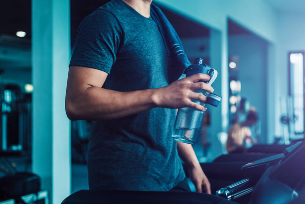 young man running on treadmill at gym and holding bottle of water. - Foto, immagini