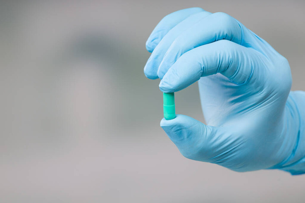 Dokters hand in medische handschoenen presenteert een medicijn pil - Foto, afbeelding