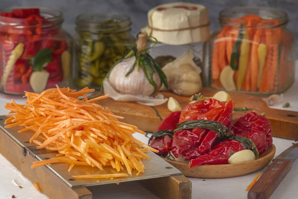 Морква натерта на ручній тертці на тлі диференційованих продуктів - перець, часник, морква на легкому дерев'яному столі
 - Фото, зображення
