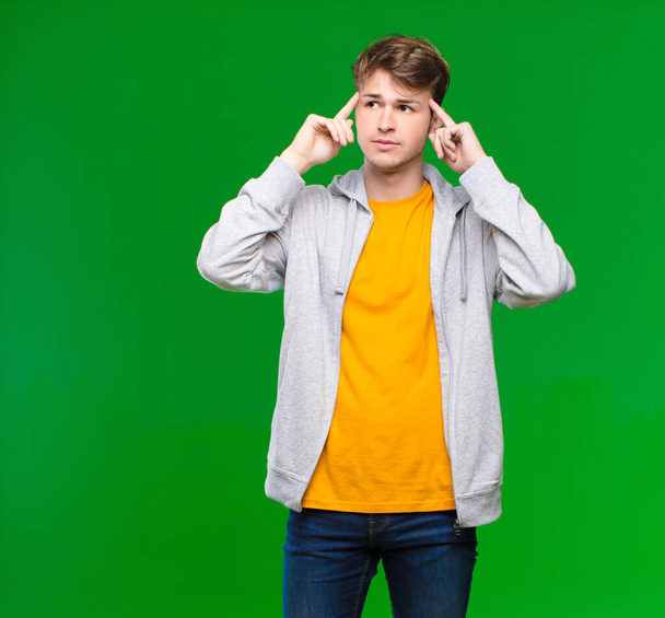 young blonde man feeling confused or doubting, concentrating on an idea, thinking hard, looking to copy space on side against chroma key wall - Foto, afbeelding