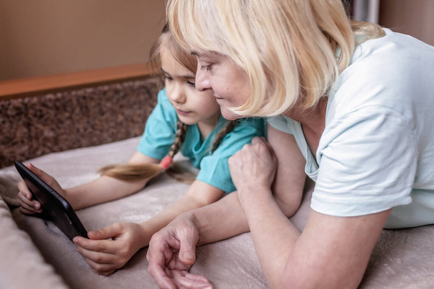 Heureux petit-enfant enseignant à sa grand-mère à utiliser une tablette portative et à faire du selfie, la vie en ligne, nouvelle normale après une pandémie de coronavirus, heureux surfeur d'argent une génération indigène numérique
 - Photo, image