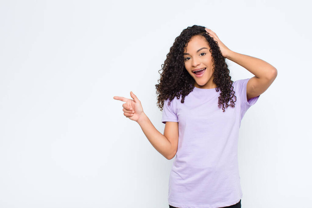 young black woman laughing, looking happy, positive and surprised, realizing a great idea pointing to lateral copy space against white wall - Foto, Imagem