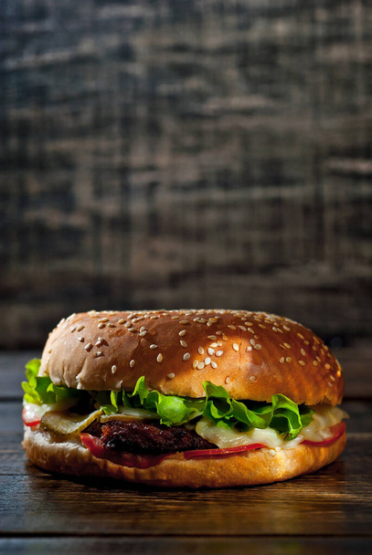 Burger on a dark wooden board. Cheeseburger with cutlet and herbs on black background. Food with contrasting dramatic light. Free space for text. - Foto, afbeelding