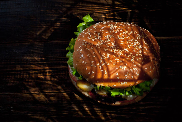 Burger on a dark wooden board. Cheeseburger with cutlet and herbs on black background. Food with contrasting dramatic light. Free space for text. - Фото, зображення