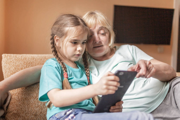 幸せな孫は、ポータブルタブレットを使用し、セルフィーを作るために彼女の祖母を教えて,オンライン生活,コロナウイルスパンデミック後の新しい正常な,幸せな銀サーファーデジタルネイティブ世代 - 写真・画像