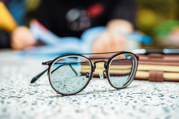 Glasses on the ground near a book and blur student reading a book back. - Foto, afbeelding