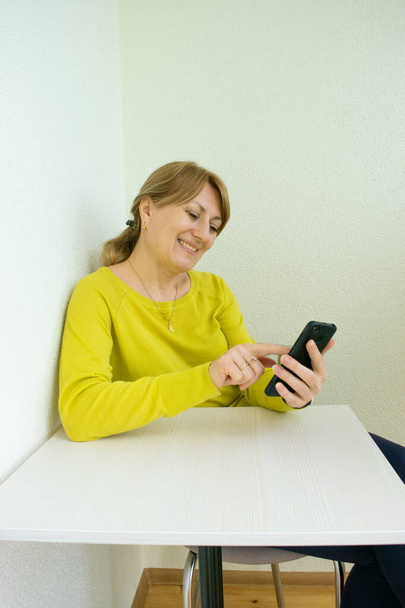 Усміхнена жінка зі смартфоном спілкується в онлайн-чаті та соціальних мережах, перебуваючи вдома на білій логігії під час карантинної та соціальної відстані від Coronovirus pandemic. Домашній відпочинок. - Фото, зображення
