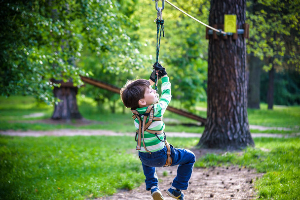 Lächelnder Junge reitet Seilrutsche. Glückliches Kind an der Seilrutsche. Das Kind passiert den Seil-Hindernisparcours. - Foto, Bild