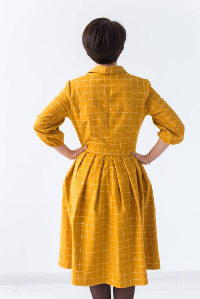 clothing, designer, people concept - back view of attractive woman in a yellow dress posing on white room. - Photo, Image