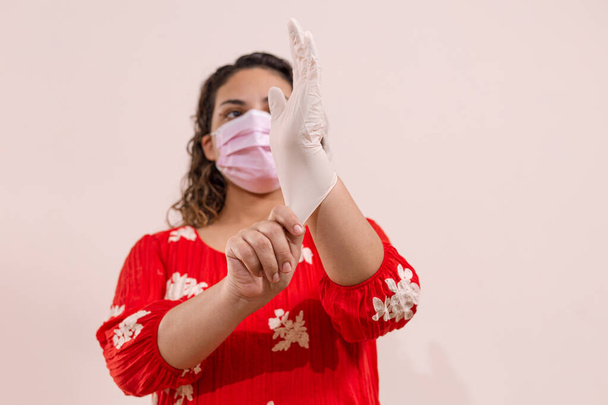 Mujer latina con vestido rojo tomando precauciones por el Covid-19 usando una mascarilla, guantes y un atomizador con alcohol para prevenir infeccion del coronavirus en el 2020 - Photo, image