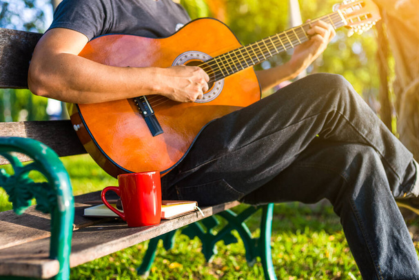 cup of coffee on wood bench near people play guitar in the park. - Foto, Imagen