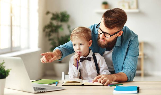 Молодой бородатый мужчина в очках указывает на ноутбук, объясняя урок маленькому сыну во время совместной онлайн-учебы в хоме
 - Фото, изображение
