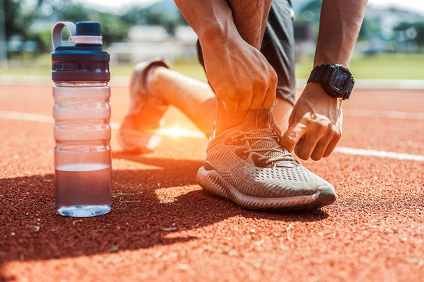 Man hands tying shoelaces and water bottle near him on red stadium track. Preparation for running. - Fotoğraf, Görsel