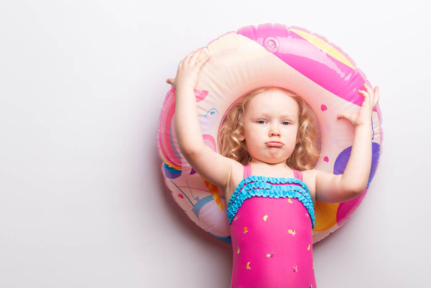 Caucasian curly girl with an upset sad face in a swimsuit with a rubber ring on a white background.Coronavirus situation. Stay at home - Φωτογραφία, εικόνα