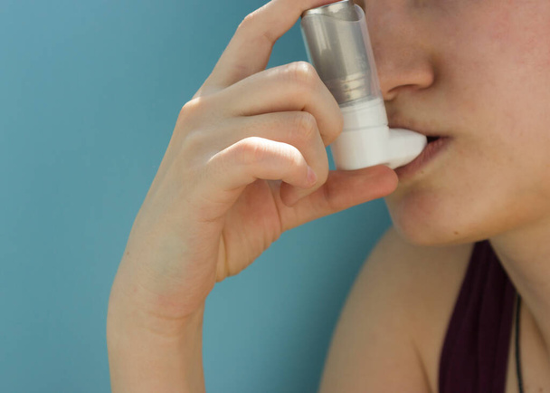 Всемирный день астмы 5 мая ингалятор против астмы на синем фоне. Подросток использует ингалятор
. - Фото, изображение
