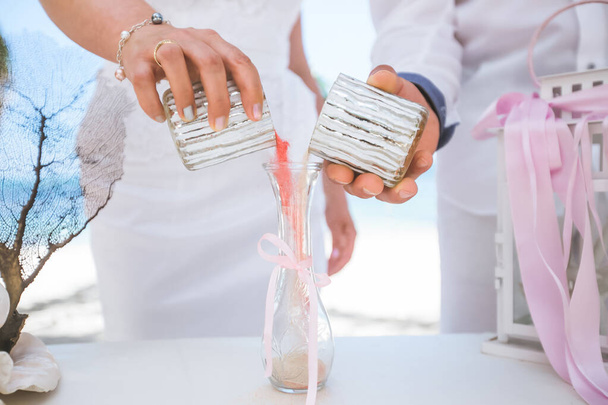 Bride and groom pouring colorful different colored sands into the crystal vase close up during symbolic nautical decor destination wedding marriage ceremony on sandy beach in front of the ocean in Punta Cana, Dominican republic - Fotografie, Obrázek
