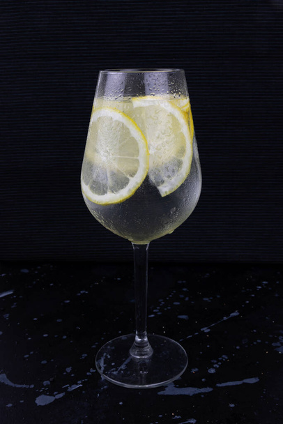 Przezroczysta szklanka zimnej wody z plastrami cytryny na czarnym tle, letnie orzeźwienie, świeży napój, nawilżenie zdrowe - Zdjęcie, obraz