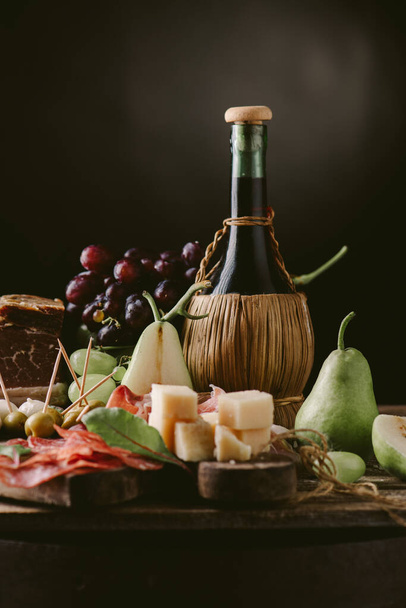 Appetizers - tomato, meat and cheese - on wooden board with flask of wine. Toned image  - Foto, afbeelding