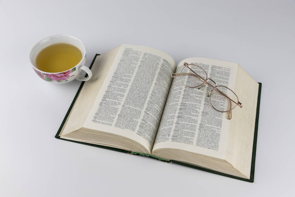 Livre ouvert, verres vintage et une tasse de thé sur fond blanc. Temps libre, détente, lecture
 - Photo, image
