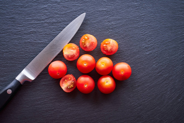 Top view of some cherry tomatoes with a knife on a dark table. Concept of vegetarian and healthy food. - Foto, imagen