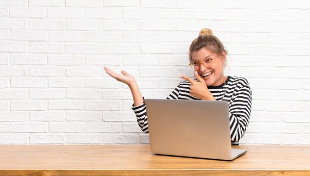 young pretty latin woman smiling cheerfully and pointing to copy space on palm on the side, showing or advertising an object sitting with her laptop - Fotografie, Obrázek