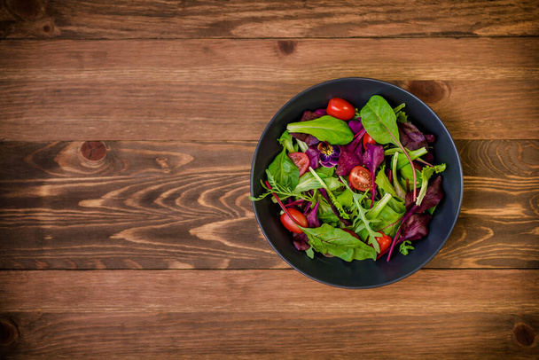 Mix of fresh green salad leaves with lettuce, spinach and beets. Salad with tomato cherry and violet on wooden rustic background. - Photo, Image