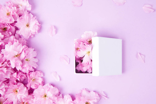 Beautiful violet pink flowers and gift box with sakura liyng on the pink background - Photo, Image