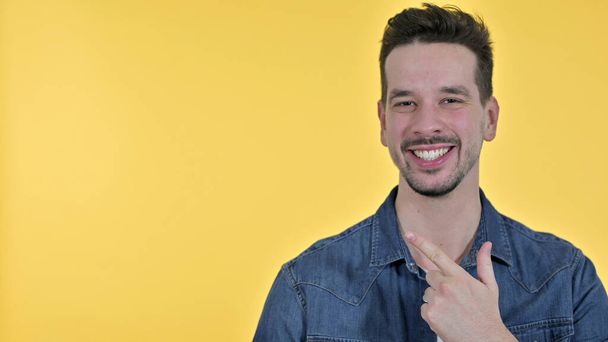 Glimlachende jonge man wijzend naar product, gele achtergrond - Foto, afbeelding