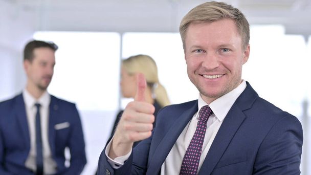 Vrolijke zakenman toont duimen in het kantoor - Foto, afbeelding